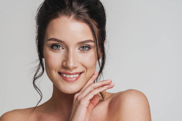Smiling young topless white woman with brown hair pulled up posing over gray background - Foto, Imagem