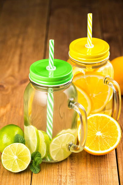 Two jars of detox water with slices of orange and lime. Glass jars with handles, lids and straws. The jars stands on a wooden table. - Φωτογραφία, εικόνα