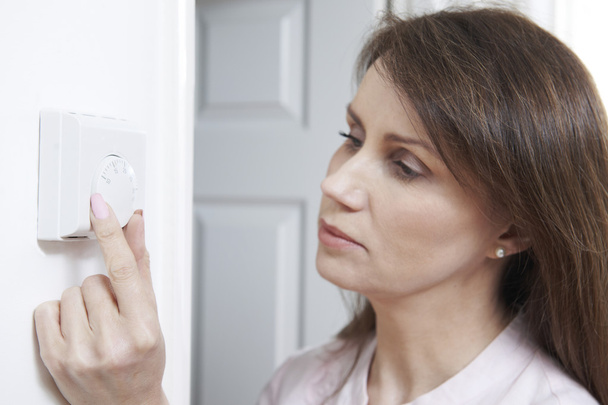 Woman Adjusting Thermostat On Central Heating Control - 写真・画像