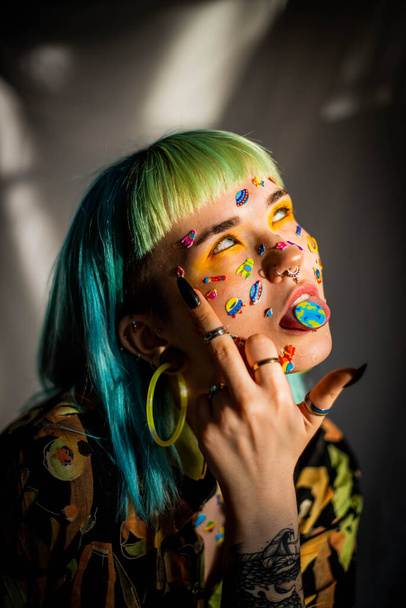 Closeup fashion portrait young pretty beautiful girl with green and blue hair. Beautiful fashion girl with luxury professional makeup and funny emoji stickers glued on the face. Young woman - Photo, Image