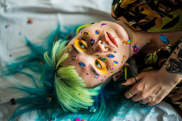 Closeup fashion portrait young pretty beautiful girl with green and blue hair. Beautiful fashion girl with luxury professional makeup and funny emoji stickers glued on the face. Young woman - Foto, Imagem