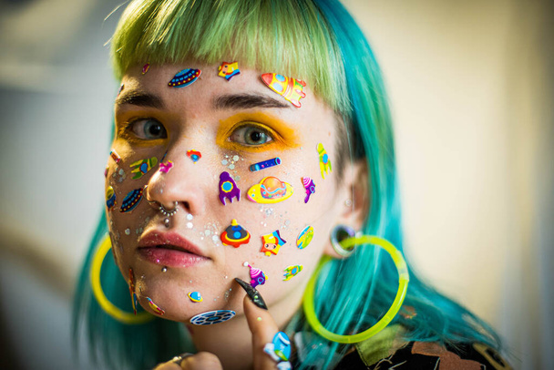 Closeup fashion portrait young pretty beautiful girl with green and blue hair. Beautiful fashion girl with luxury professional makeup and funny emoji stickers glued on the face. Young woman - Zdjęcie, obraz