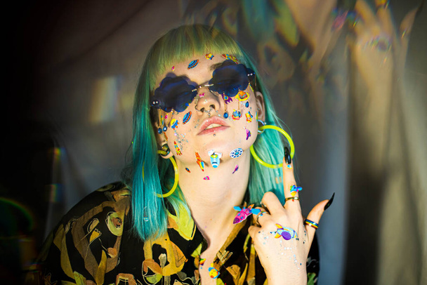 Closeup fashion portrait young pretty beautiful girl with green and blue hair. Beautiful fashion girl with luxury professional makeup and funny emoji stickers glued on the face. Young woman sunglasses - Photo, image