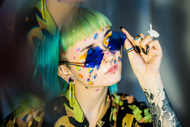 Closeup fashion portrait young pretty beautiful girl with green and blue hair. Beautiful fashion girl with luxury professional makeup and funny emoji stickers glued on the face. Young woman sunglasses - 写真・画像