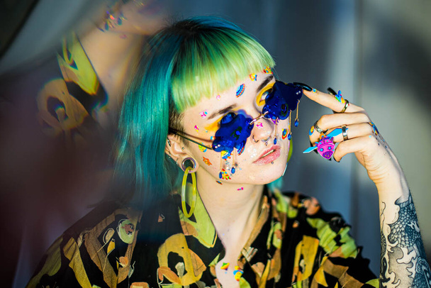 Closeup fashion portrait young pretty beautiful girl with green and blue hair. Beautiful fashion girl with luxury professional makeup and funny emoji stickers glued on the face. Young woman sunglasses - Photo, Image