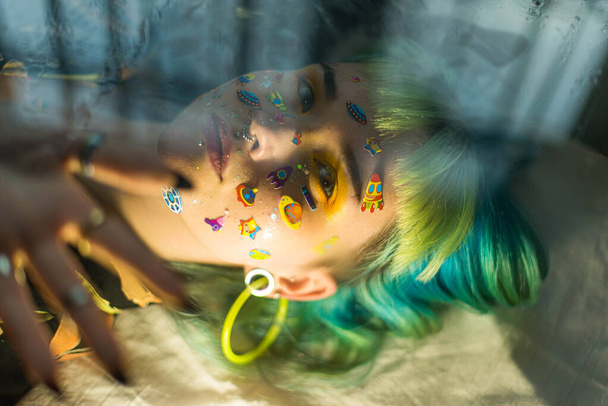 Closeup retrato de moda jovem menina bonita bonita com cabelo verde e azul. Menina de moda bonita com maquiagem profissional de luxo e adesivos emoji engraçados colados no rosto. Jovem mulher - Foto, Imagem