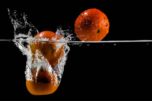 three tangerines fall into the water on a black background, copy space - Foto, Imagen
