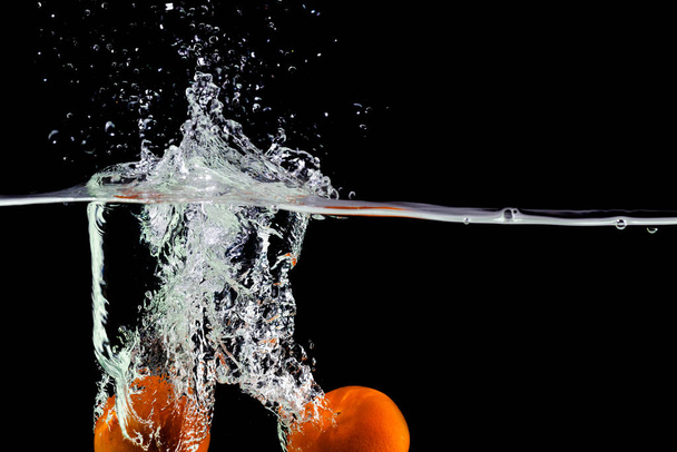 two tangerines fall into the water on a black background, copy space - Foto, afbeelding