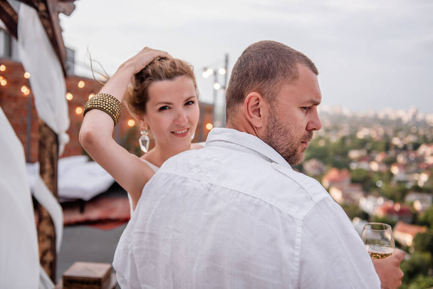 Fashion stylish woman looks over the shoulder of young man, hugs, laughs. Loving couple on the roof of the house celebrate the anniversary, romantic date. Stylish rooftop party in Moroccan interior - Photo, Image