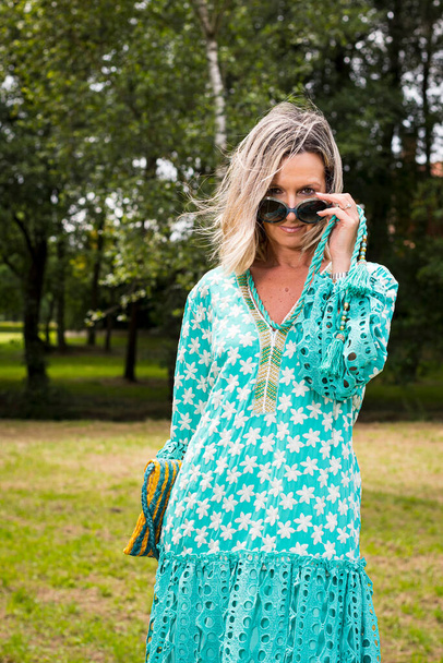 Blond model poserend in een mooie groene jurk en kijkend naar de camera onder haar zonnebrillen.De foto is genomen in een park in Asturië, Spanje.De foto heeft een achtergrond vervaging. - Foto, afbeelding