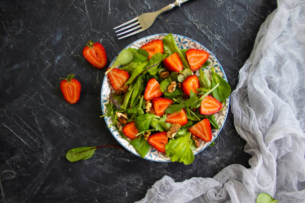 green lettuce leaves, strawberries, nuts on a plate - Fotó, kép
