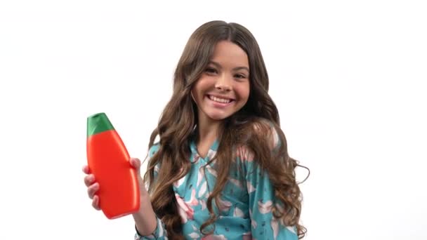 Mädchen dreht sich mit glücklichem Gesicht und hält Shampoo in der Hand, das ihr langes welliges windiges Haar berührt, Keratin. - Filmmaterial, Video