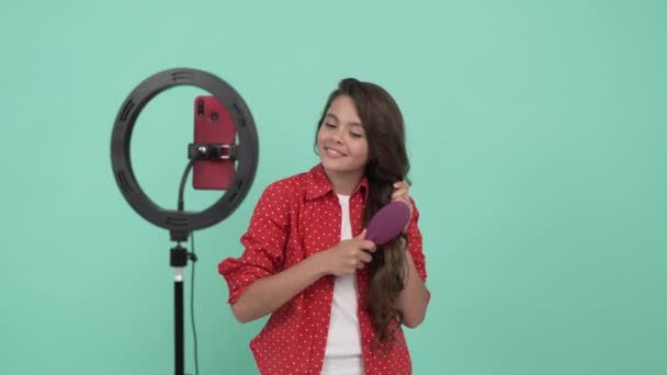 sonriente bloguera de belleza infantil promoviendo cepillo para el cabello y peinando su cabello ondulado largo, promoción - Metraje, vídeo
