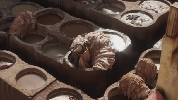 Рабочий вытаскивает кожу из чана с краской на солярии. Традиционный ручной процесс на старой фабрике. Моррелло, Африка - Кадры, видео