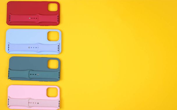 Colored silicone phone cases, complete with watch strap. Set. Up to date technology. Flat lay of diverse personal accessory laying on the yellow background. Space for text - Photo, Image