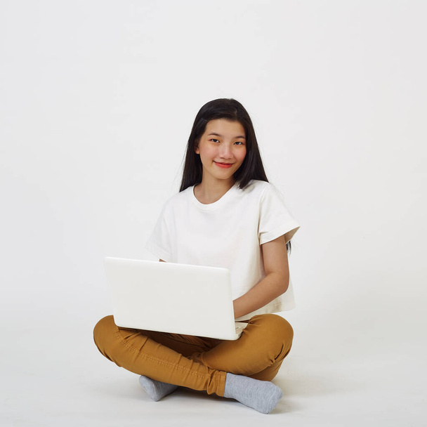 Улыбающаяся азиатка работает на ноутбуке, сидя на полу со скрещенными ногами - Фото, изображение