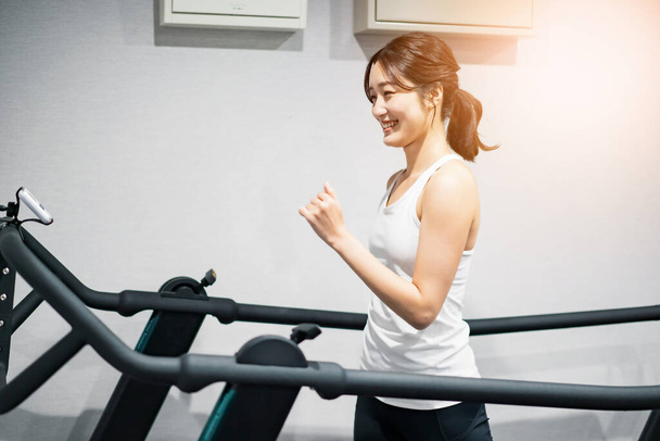 Koşu bandında egzersiz yapan Asyalı genç bir kadın. - Fotoğraf, Görsel