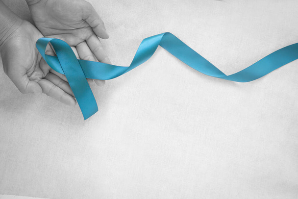 Hands holding teal color ribbon on white fabric with copy space. Ovarian Cancer Awareness, Gynecological, Uterine Cancer, Vulvar Cancer, Panic Disorder, Post Traumatic Stress Disorder (PTSD). - Photo, Image