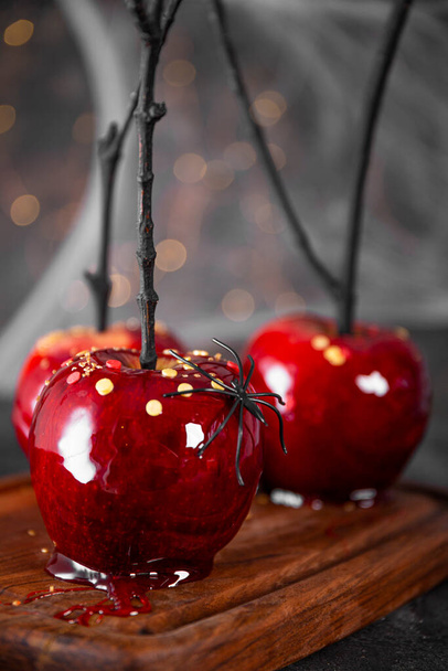  Manzanas rojas en caramelo con una decoración festiva de Halloween, un regalo original para una mesa festiva de Halloween decorada con arañas y telarañas, foto vertical - Foto, imagen