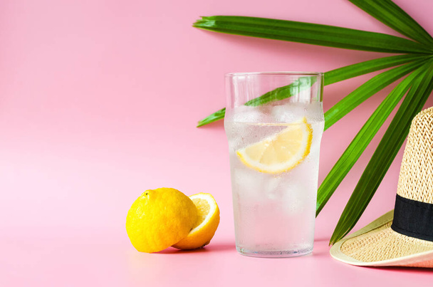 A glass of lemonade soda with hat and lady palm leaf on pink background. Summer drink concept. - Photo, Image