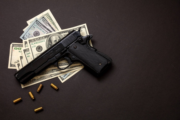 Криминальные деньги, мафия и коррупция, Концепция преступности, пистолет 9 мм и банкноты американского доллара на черном фоне. - Фото, изображение