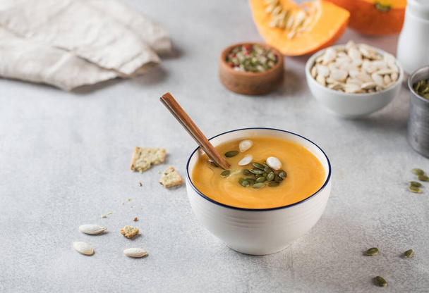 Pumpkin cream soup in a bowl with seeds on a gray background. Comfortable riding, autumn menu.  - 写真・画像