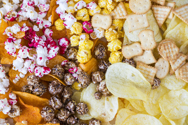 Соленый и сладкий попкорн и чипсы на белом фоне, вид под низким углом - Фото, изображение