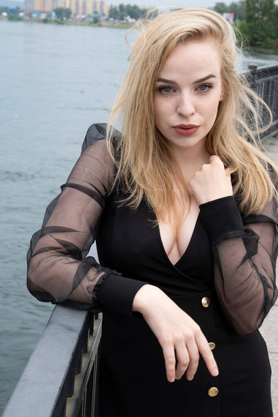 Emotional blonde in a black dress at the embankment fence - Фото, зображення