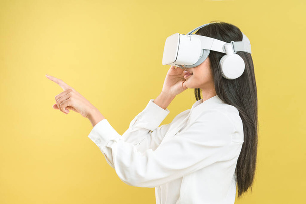 Femme asiatique portant casque VR sur fond jaune pour obtenir une expérience excitée de la technologie de réalité virtuelle, Digital 3D simulation divertissement à la maison, VR Simulator for Education concept. - Photo, image