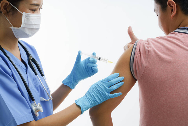 Średni portret Azjatki lekarza lub pielęgniarki w masce ochronnej i gumowych rękawiczkach podczas wstrzyknięcia leku lub szczepionki w ramię. - Zdjęcie, obraz