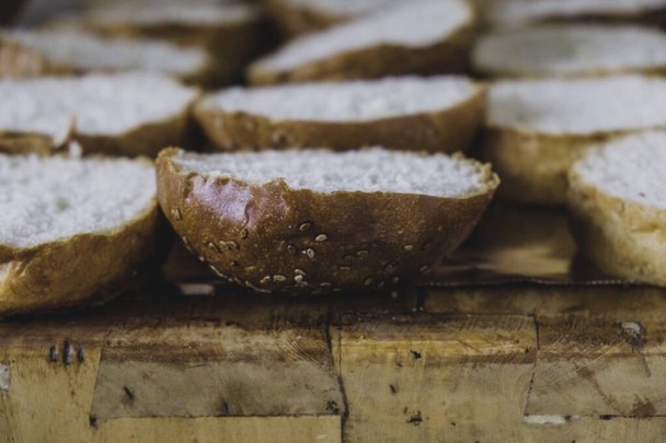 Burger ψωμί τοποθετείται σε ένα ξύλο κοπής. Κοπή του σκάφους με φέτες ψωμιού με σπόρους σουσαμιού για την παρασκευή μπιφτέκι. Σάντουιτς με σουσάμι για κιμά ή ψητό κρέας. Σάντουιτς με μαρούλι από πάνω. - Φωτογραφία, εικόνα