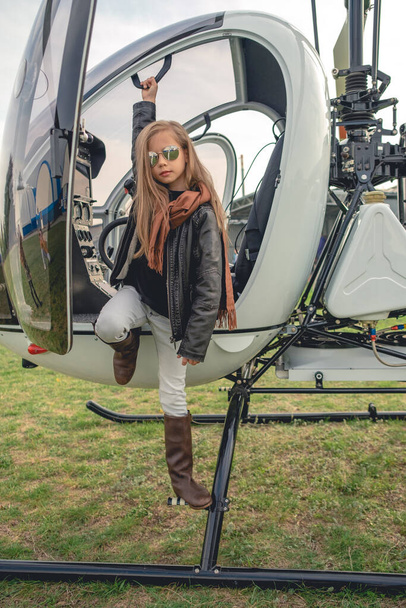 Preteen Mädchen mit verspiegelter Sonnenbrille steht auf dem Trittbrett des offenen Hubschraubers - Foto, Bild