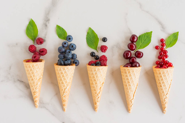 waffle cones with berries and mint leaves on a white marble table. delicious dessert. top view. - Photo, image