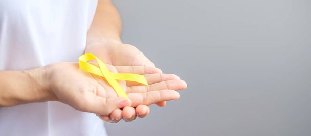 hand holding Yellow Ribbon for supporting people living and illness. September Suicide prevention day, Childhood, Sarcoma and bone cancer awareness month concept - Fotografie, Obrázek