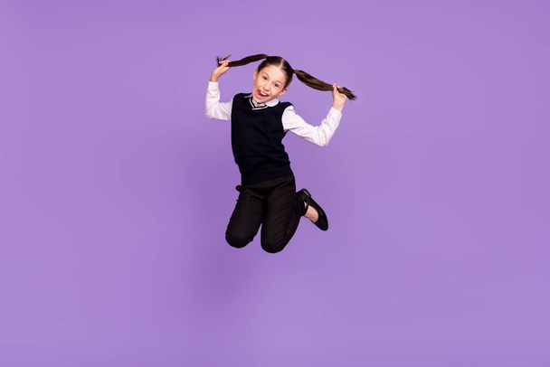 Photo of crazy childish schoolkid girl jump play ponytails show tongue wear uniform isolated violet color background. - Fotoğraf, Görsel