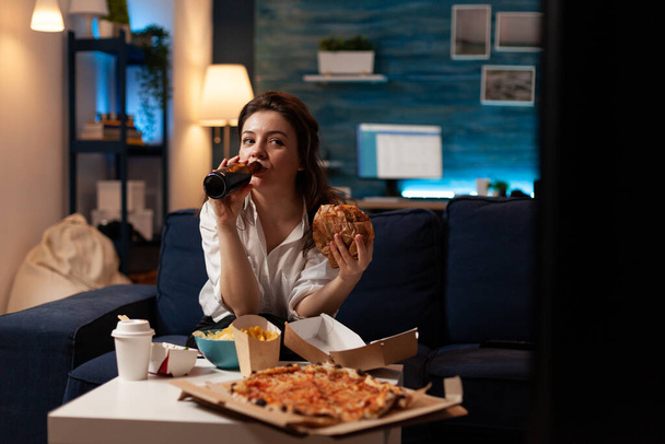 Happy woman drinking beer eating tasty delicious burger watching documentary series movie - Photo, Image