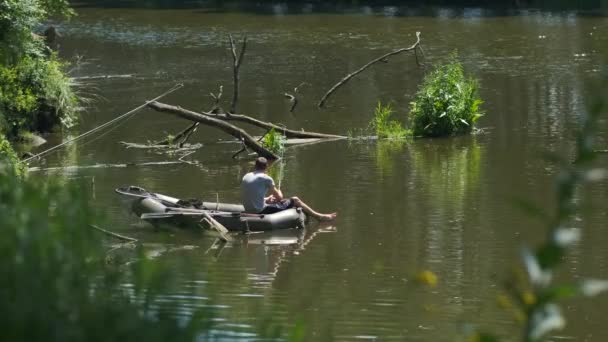 Genç bir adam nehirde kauçuk bir teknede olta ile balık tutuyor. Doğada dinlenme ve balık tutma kavramı. - Video, Çekim