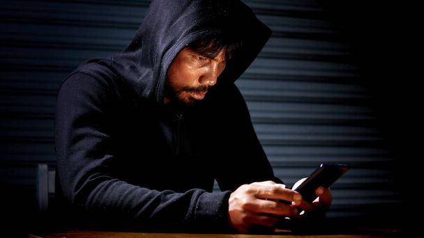 Mysterious man in hoodie on dark background. Dangerous criminal. Silhouette of man in the hood, dark mysterious man hoodie, murderer, hacker, anonymus on the black background with free space - Foto, Imagen