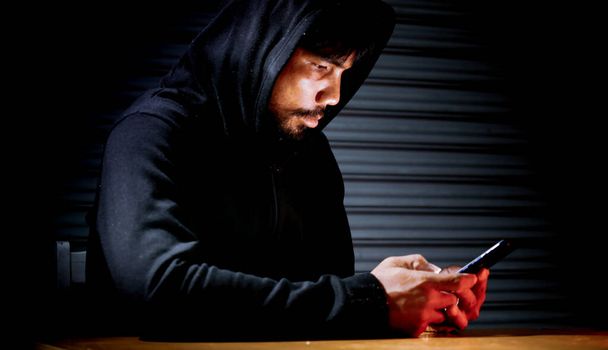Mysterious man in hoodie on dark background. Dangerous criminal. Silhouette of man in the hood, dark mysterious man hoodie, murderer, hacker, anonymus on the black background with free space - Photo, Image