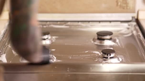 Keittiössä oleva mies pesee kaasulieden, kädet kumikäsineissä erityisten puhdistusaineiden avulla ja sieni poistaa lian kaasulieden pinnalta.. - Materiaali, video