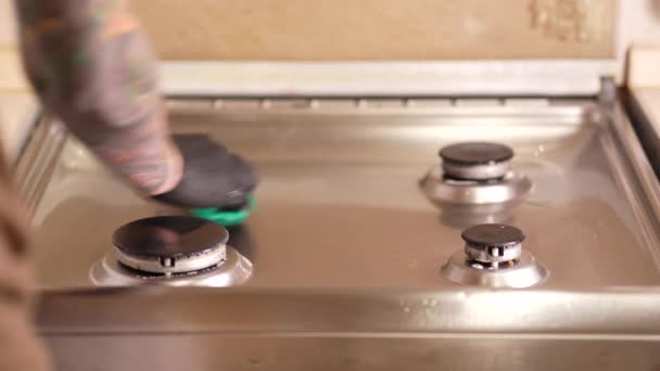 Mężczyzna w kuchni myje kuchenkę gazową, ręce w gumowych rękawiczkach za pomocą specjalnych środków czyszczących, a gąbka usuwa brud z powierzchni pieca do gotowania.. - Materiał filmowy, wideo