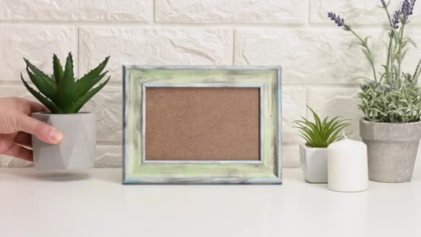 empty white wooden photo frame and flowerpots with plants on white table, white background. Woman's hand puts pots of succulents on the table - Footage, Video