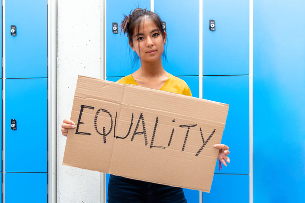 Teen asiatisches Mädchen, das in der High School ein Transparent mit einem rachsüchtigen Gleichheitszeichen in die Kamera hält. Gleichberechtigungskonzept. - Foto, Bild