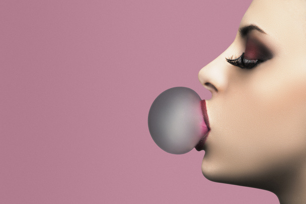 Krásná žena s perfektní make-up foukání růžové bubliny žvýkačky. Detailní portrét na růžovém pozadí s kopírovacím prostorem - Fotografie, Obrázek