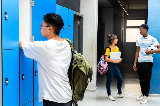 十代のアジアの高校生はロッカーに本を置いています。学校の廊下で話してる10代の若者。学校のコンセプトに戻る. - 写真・画像