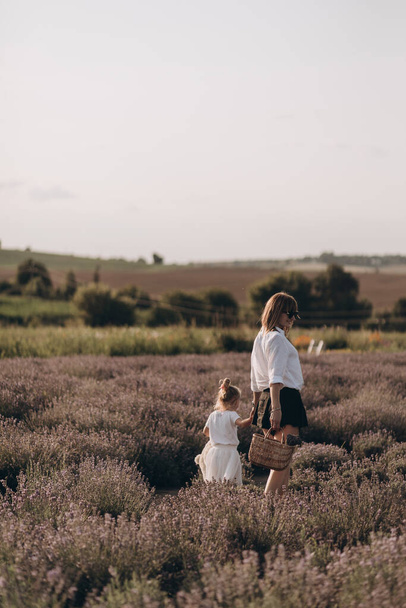 Moeder en baby meisje wandelen in lavander veld, knuffelen en plezier hebben buiten in de natuur - Foto, afbeelding