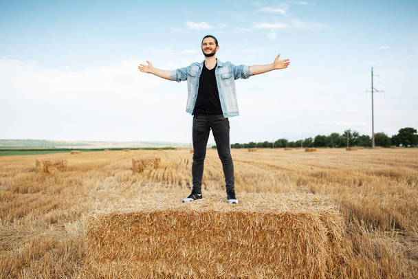 Buğday tarlasında samanlıklarda elleri havada genç mutlu bir adam.. - Fotoğraf, Görsel