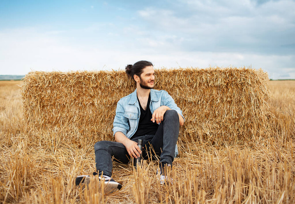Genç adam buğday tarlasında samanlıkların arkasında oturuyor.. - Fotoğraf, Görsel