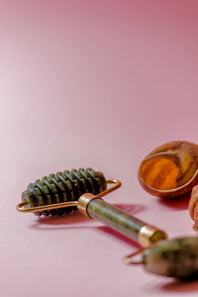 Masajeador depurador de jade y masajeador facial de rodillos sobre un fondo rosa junto a conchas marinas marrones. - Foto, imagen