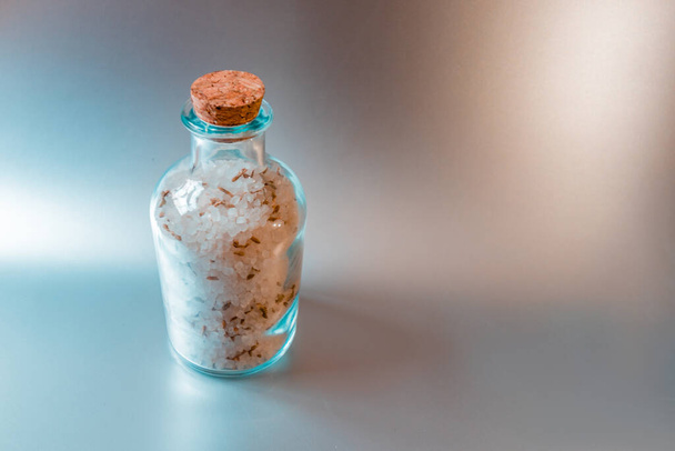 Un gran contenedor de vidrio cerrado con sal blanca marina se encuentra sobre un fondo de cocina ligero. - Foto, imagen